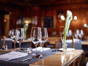 A restaurant setting with a table set for dining, featuring wine glasses, a vase with a flower, and a candle. - Boutique Hotel Schluessel (Beckenried)