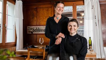 A restaurant interior with wooden paneled walls, a sign reading "Zum Schlüsser", and a table with a wine glass and bottle.