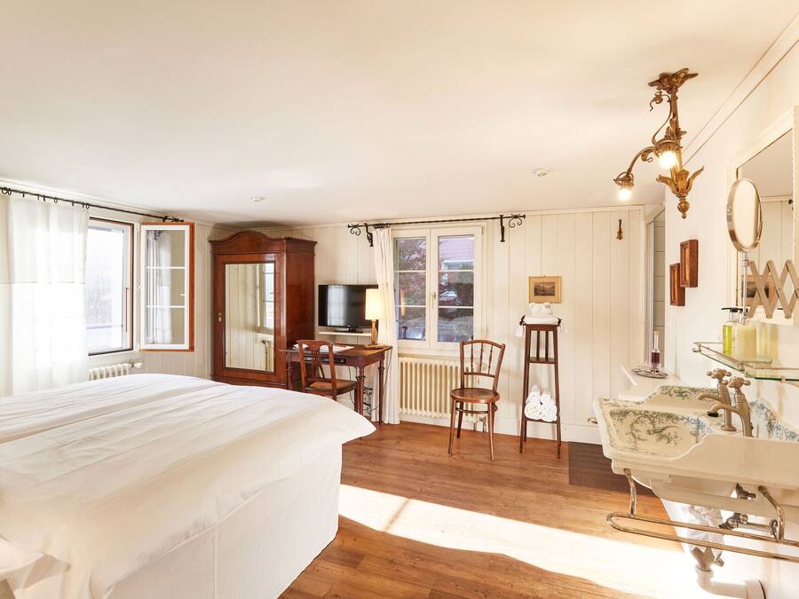 A bedroom with a large bed, a desk, a chair, a vanity with a mirror, and a television.