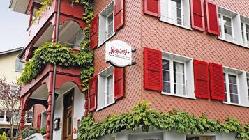 Un edificio rojo y blanco con un letrero que dice "Schlossel". Tiene un balcón con persianas rojas y follaje.