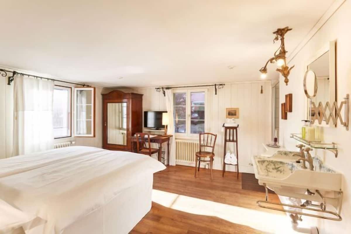 Ein Hotelzimmer mit einem großen Bett, einem Schreibtisch mit Stuhl, einem Fernseher, einem Fenster mit Vorhängen und einem Badezimmer mit Waschbecken und Spiegel.