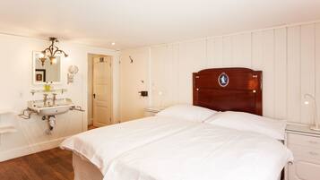 Een slaapkamer met een houten hoofdbord, een wit bed, een nachtkastje, een witte dressoir, een spiegel en een wastafel aan de muur.