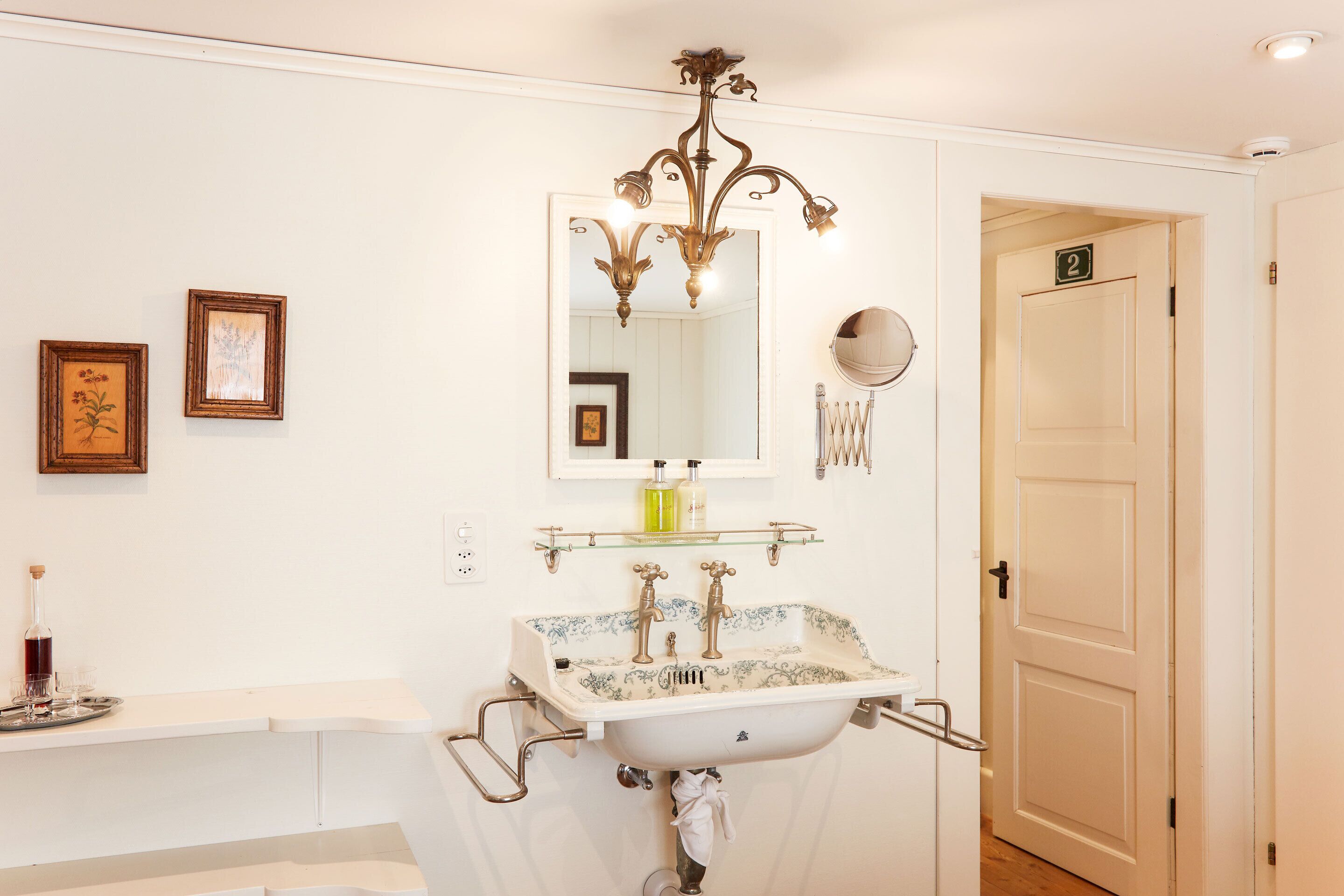 A bathroom with a white sink, a mirror, and a chandelier. There is a door with the number 2 on it.