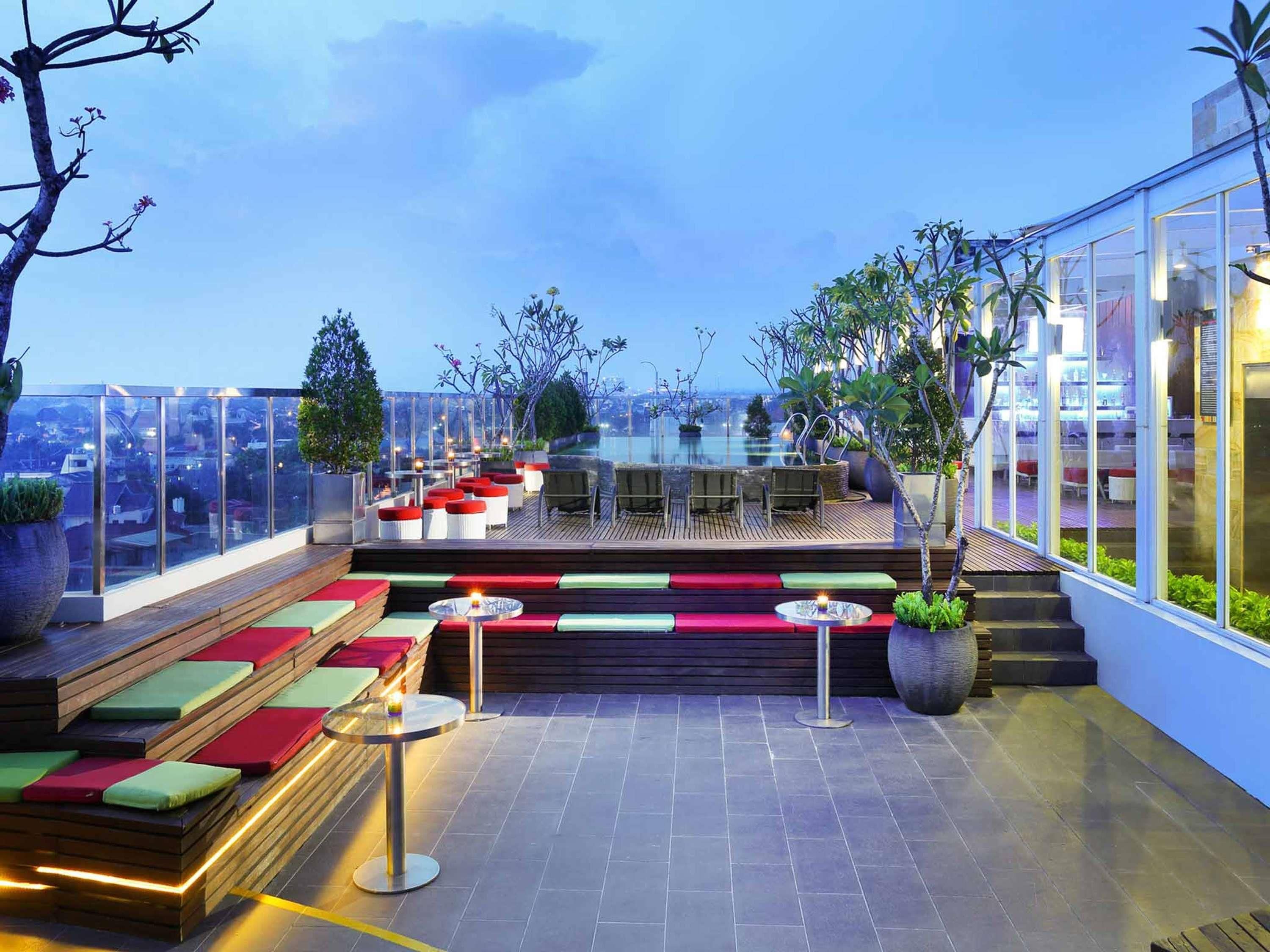 A rooftop terrace with seating areas, a glass balustrade, and a view of the cityscape.