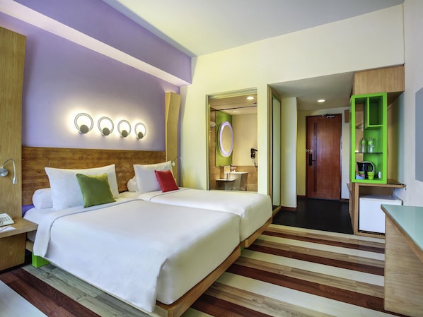Une chambre d’hôtel avec deux lits, une tête de lit en bois, une table de chevet avec un téléphone, un miroir et un meuble de rangement vert.