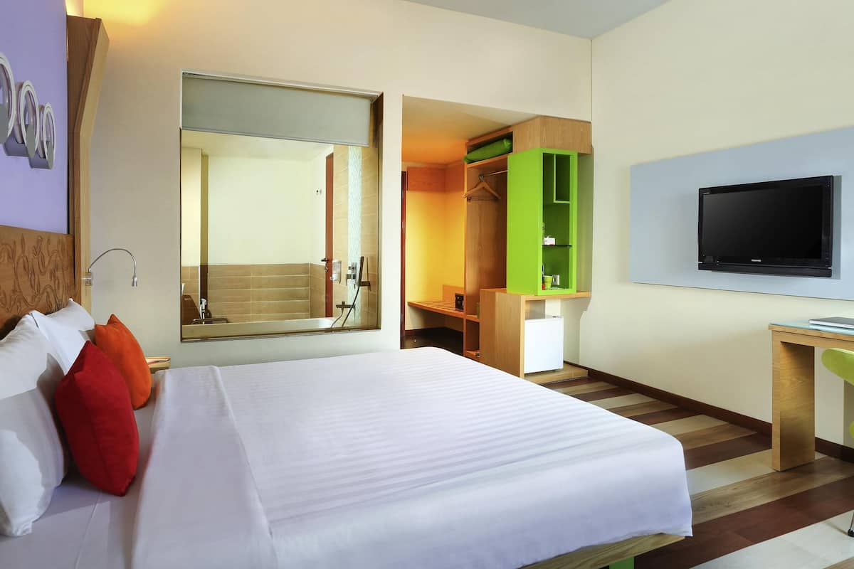 Quarto de hotel com cama, espelho, televisão, guarda-roupa e secretária.