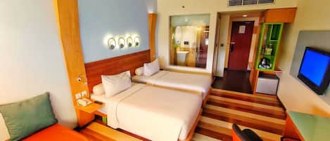 A hotel room with a large bed, a desk with a chair, a television, and a small kitchenette.