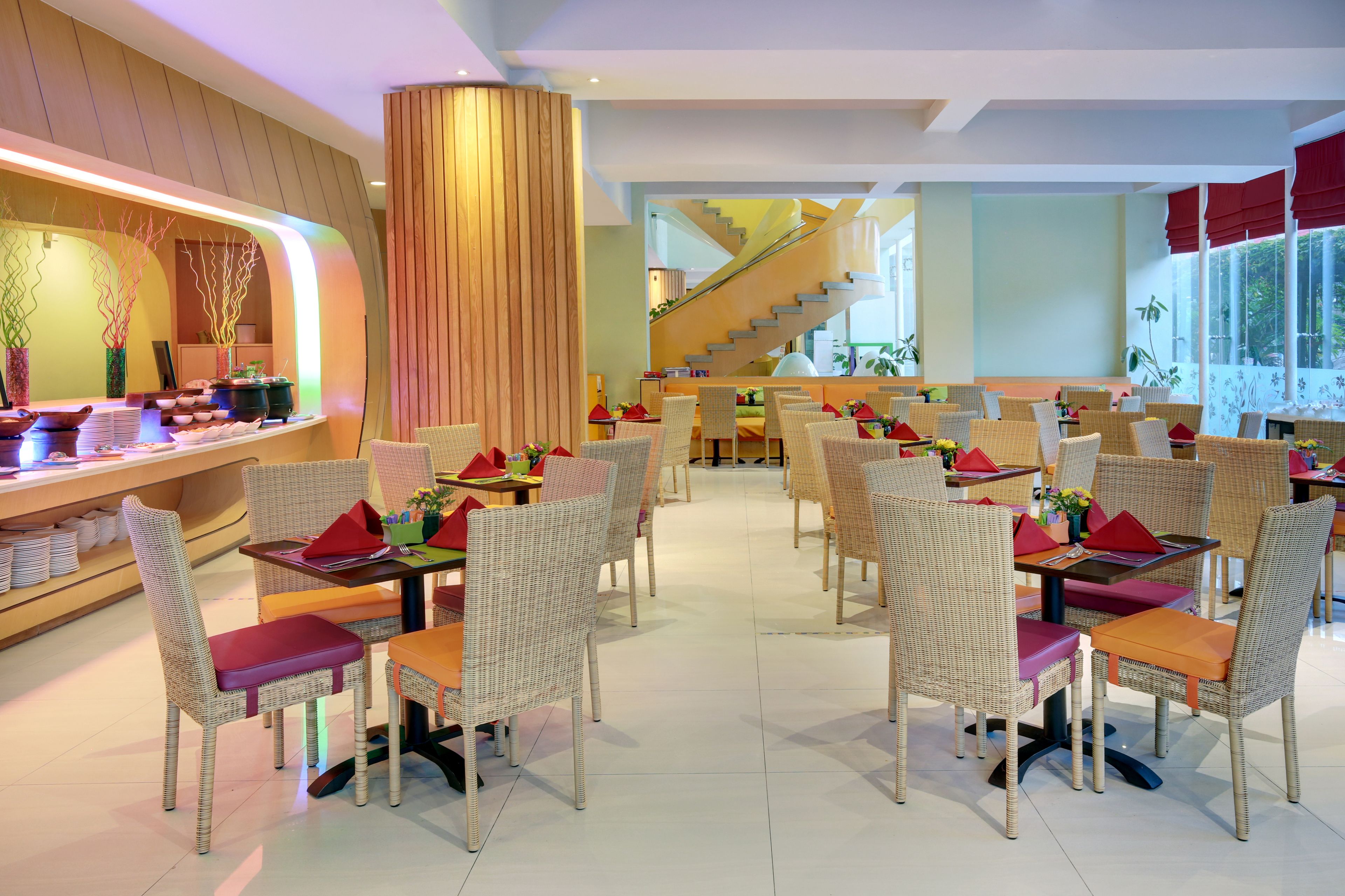 Um restaurante com cadeiras de vime, um balcão com painel de madeira e uma escadaria ao fundo.