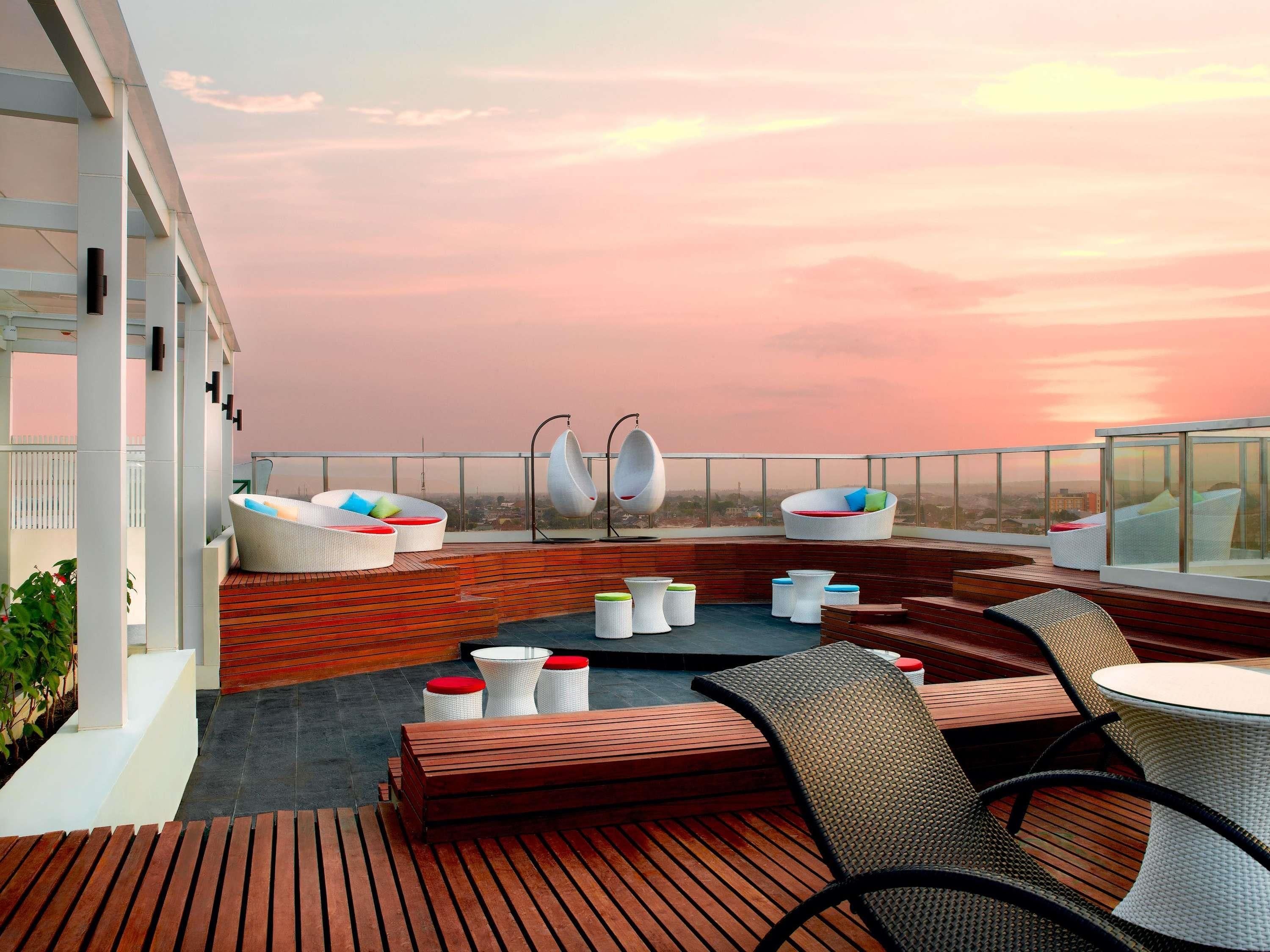 A rooftop terrace with outdoor seating, a view of the cityscape, and a sunset.