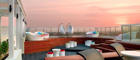 A rooftop terrace with outdoor seating, a view of the cityscape, and a sunset.