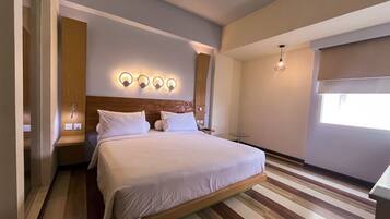 Une chambre d’hôtel moderne avec un grand lit, une tête de lit en bois et une petite table de chevet.