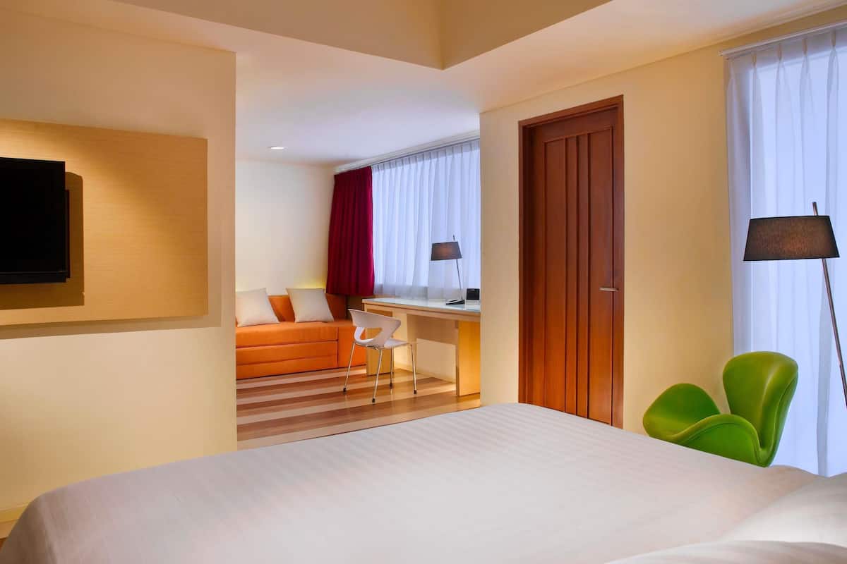 Quarto de hotel com cama, escrivaninha, cadeira, televisão e guarda-roupa.