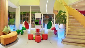 A modern indoor space with a curved staircase, colorful seating areas, and indoor plants.