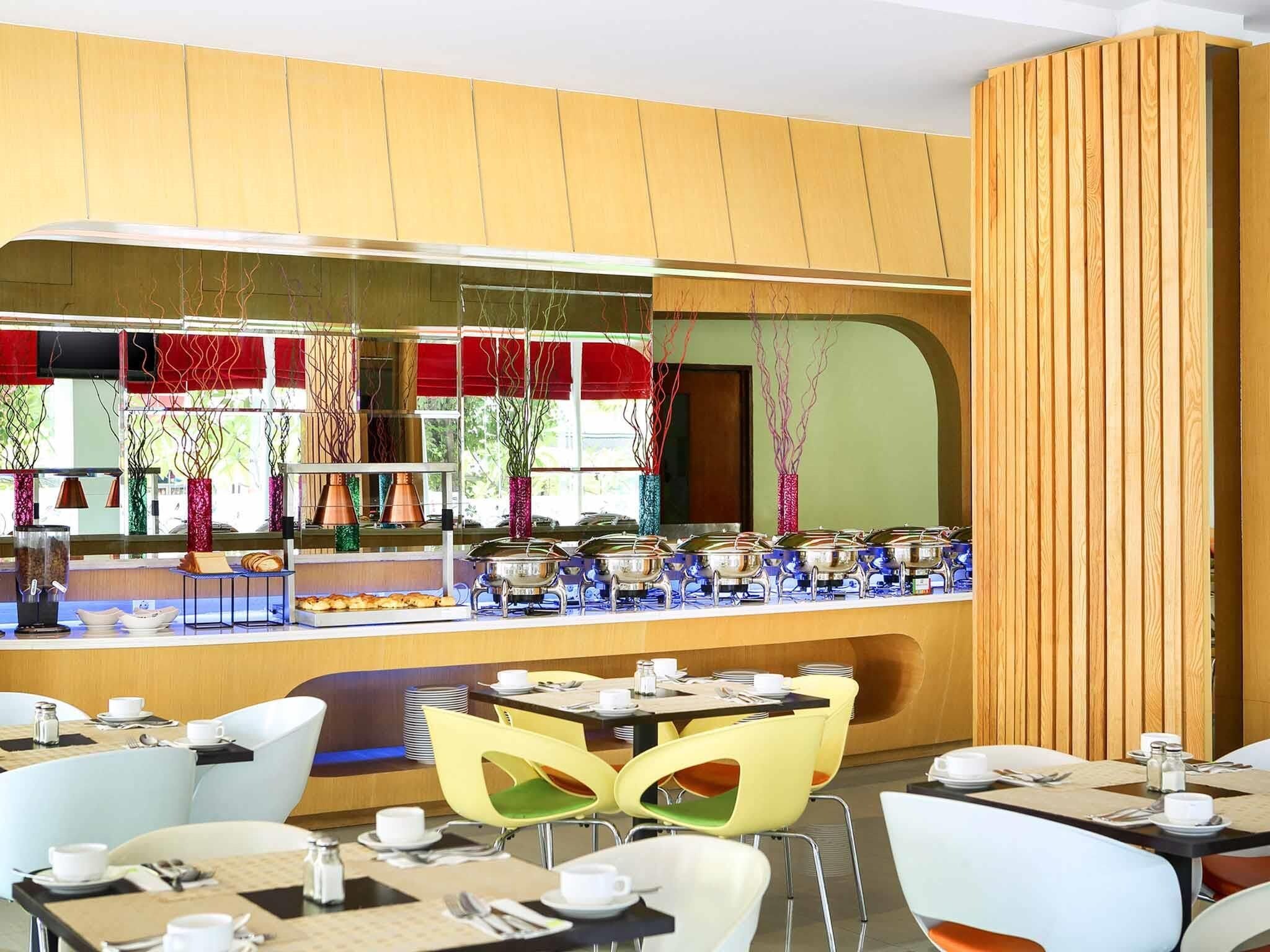Un restaurant avec un comptoir où sont exposés les plats, des chaises colorées et un mur en bois.