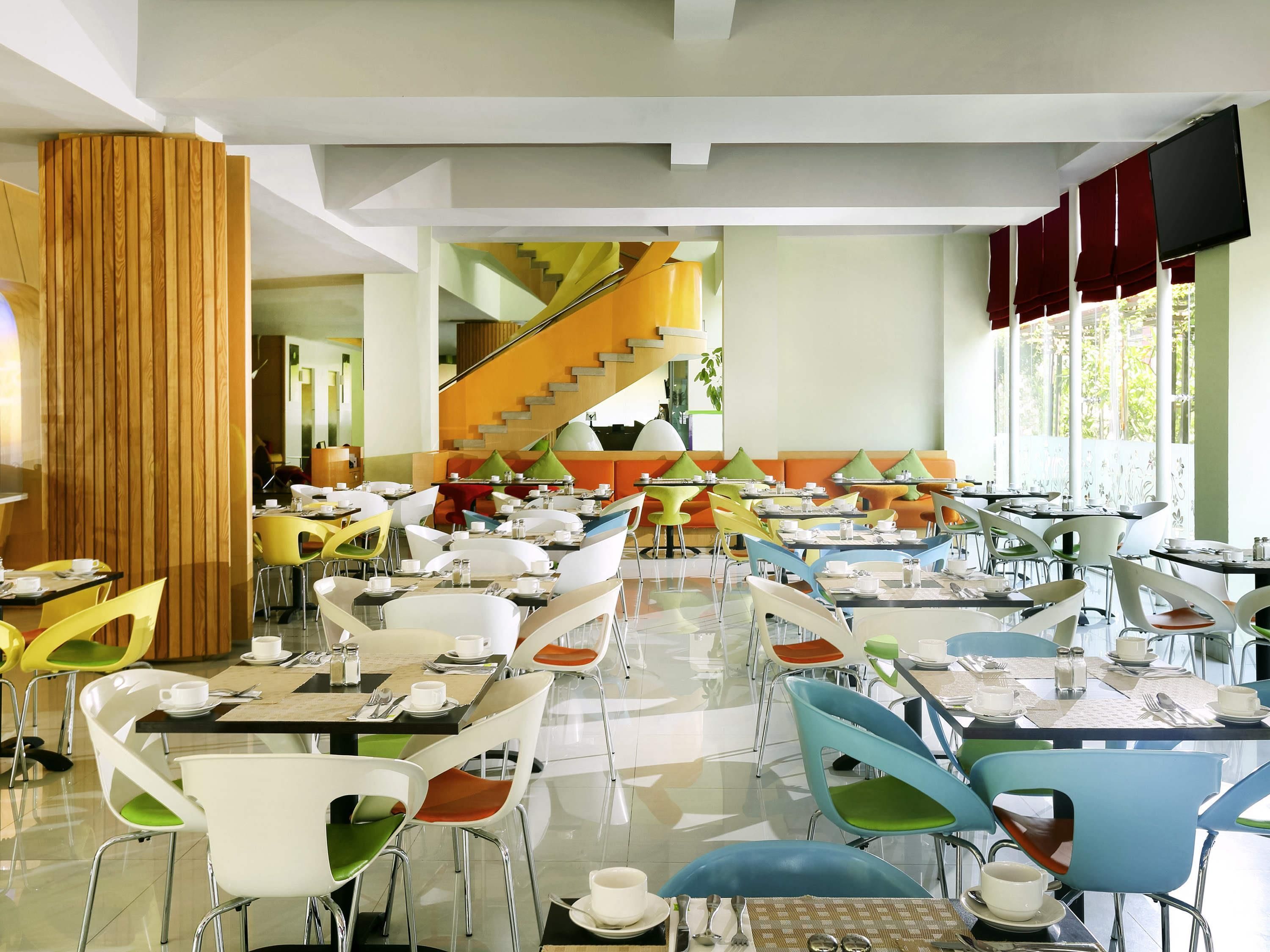A modern restaurant with multiple dining tables and chairs, a staircase, and large windows.
