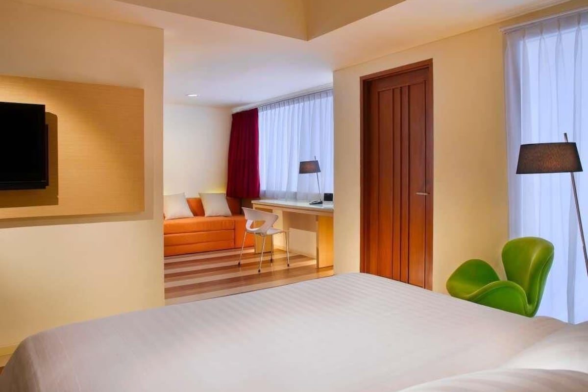 A hotel room with a bed, a desk, a chair, a TV, and a window with curtains.