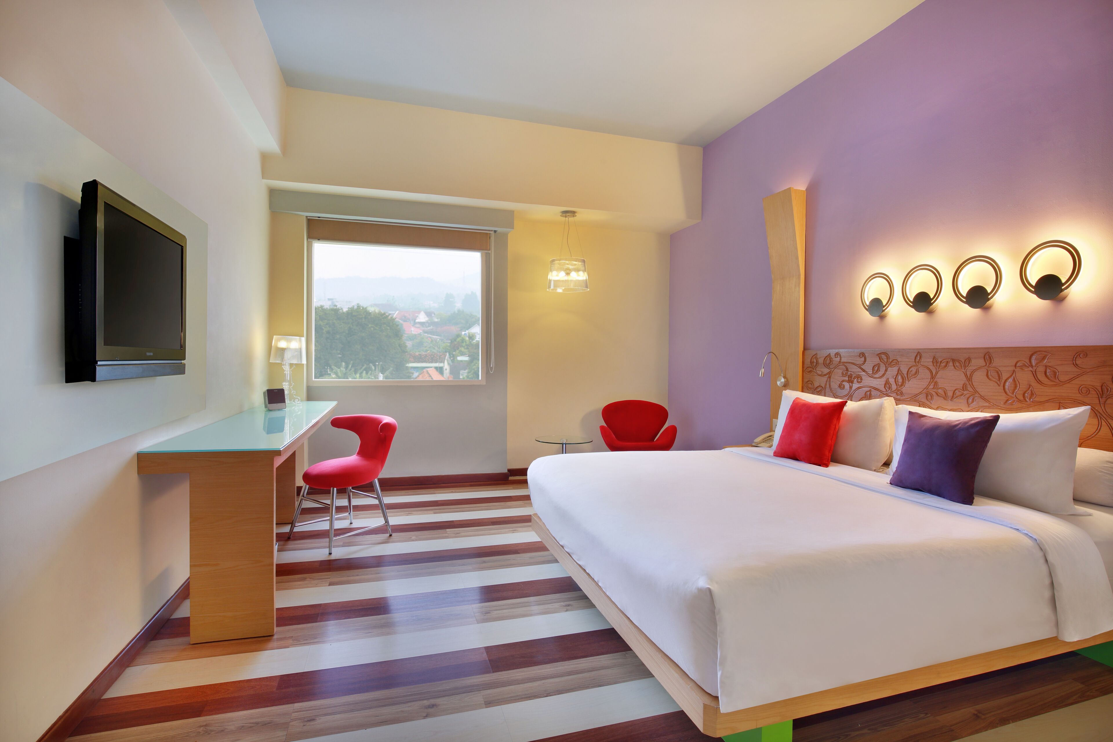 Habitación de hotel con cama, escritorio, silla, televisor y ventana con vistas.