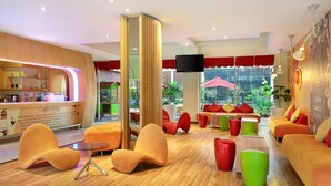 A modern lounge area with orange and red seating, a coffee station, and large windows offering a view of the outdoors.