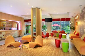 A modern lounge area with orange and red seating, a coffee station, and large windows offering a view of the outdoors.