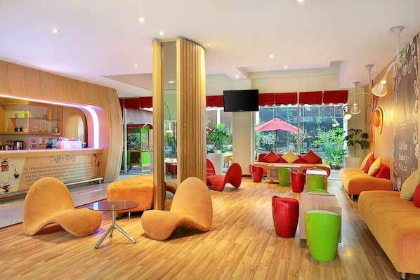 Een moderne lounge met oranje en rode zitplaatsen, een koffiehoek en grote ramen met uitzicht op het omliggende landschap.