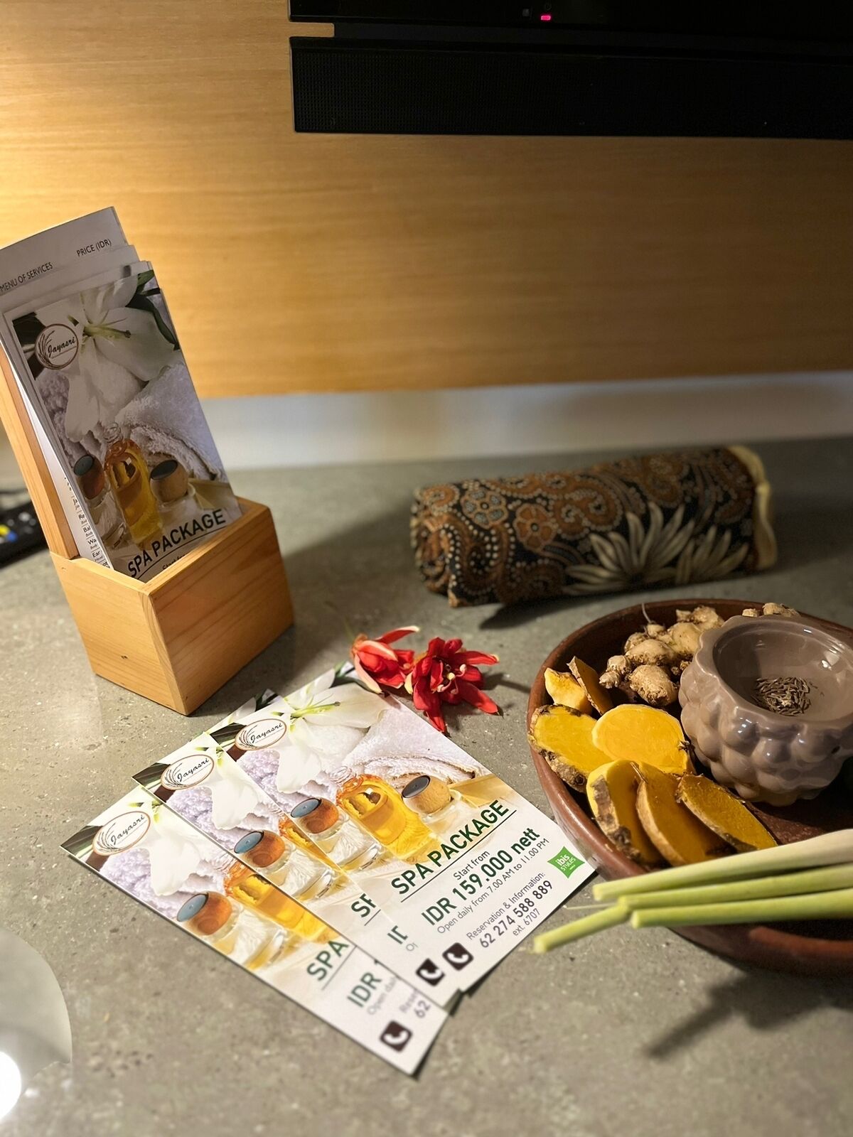 Eine Holzkiste mit einer Anzeige für ein Wellnesspaket, einem Dekoelement und einer Schüssel mit Ingwerscheiben sowie einer kleinen Dose.