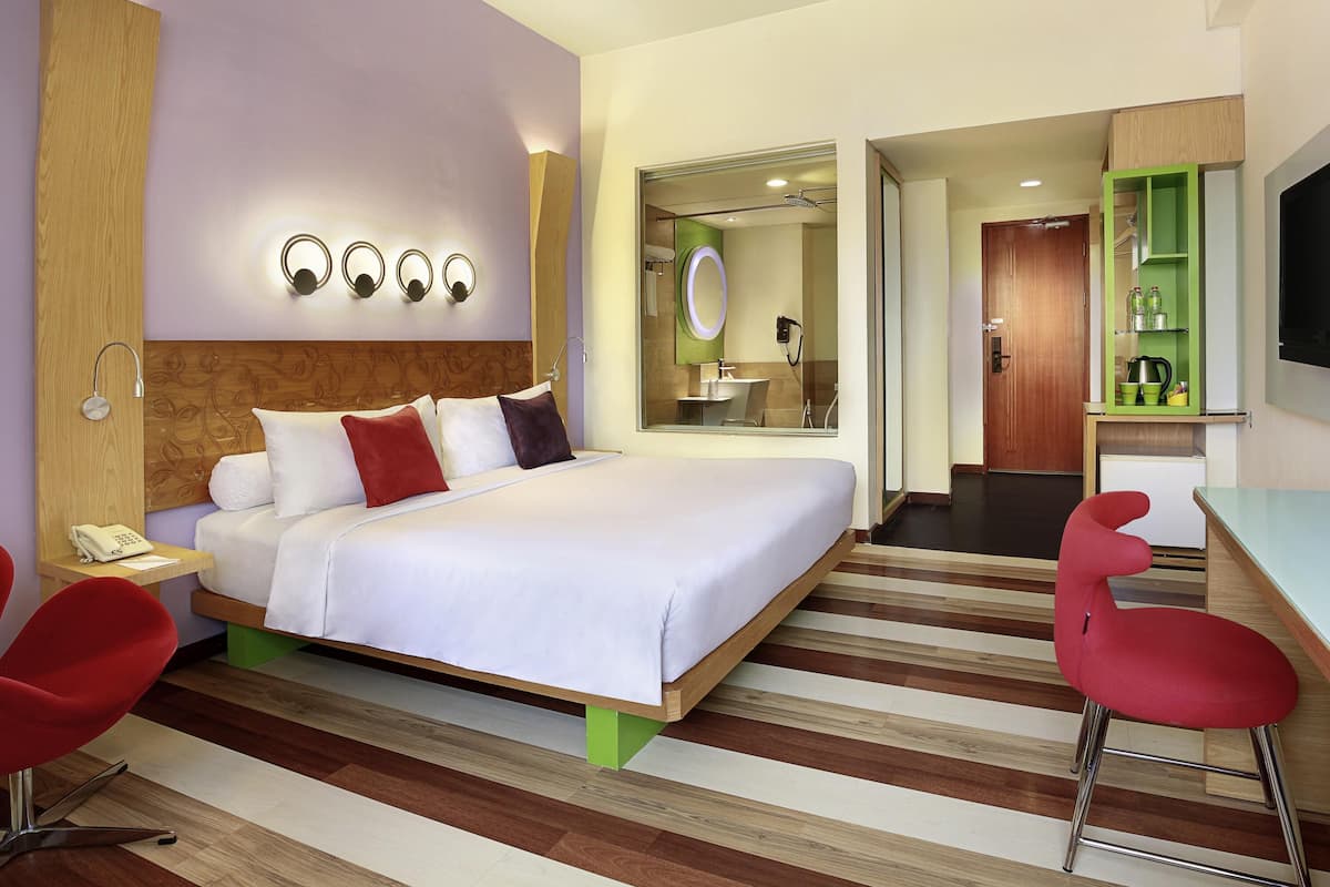 Quarto de hotel com cama, mesa de cabeceira, abajur e espelho.