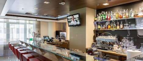 Una zona de bar con una barra alargada, taburetes rojos, una pantalla de televisión y estantes llenos de botellas y vasos.