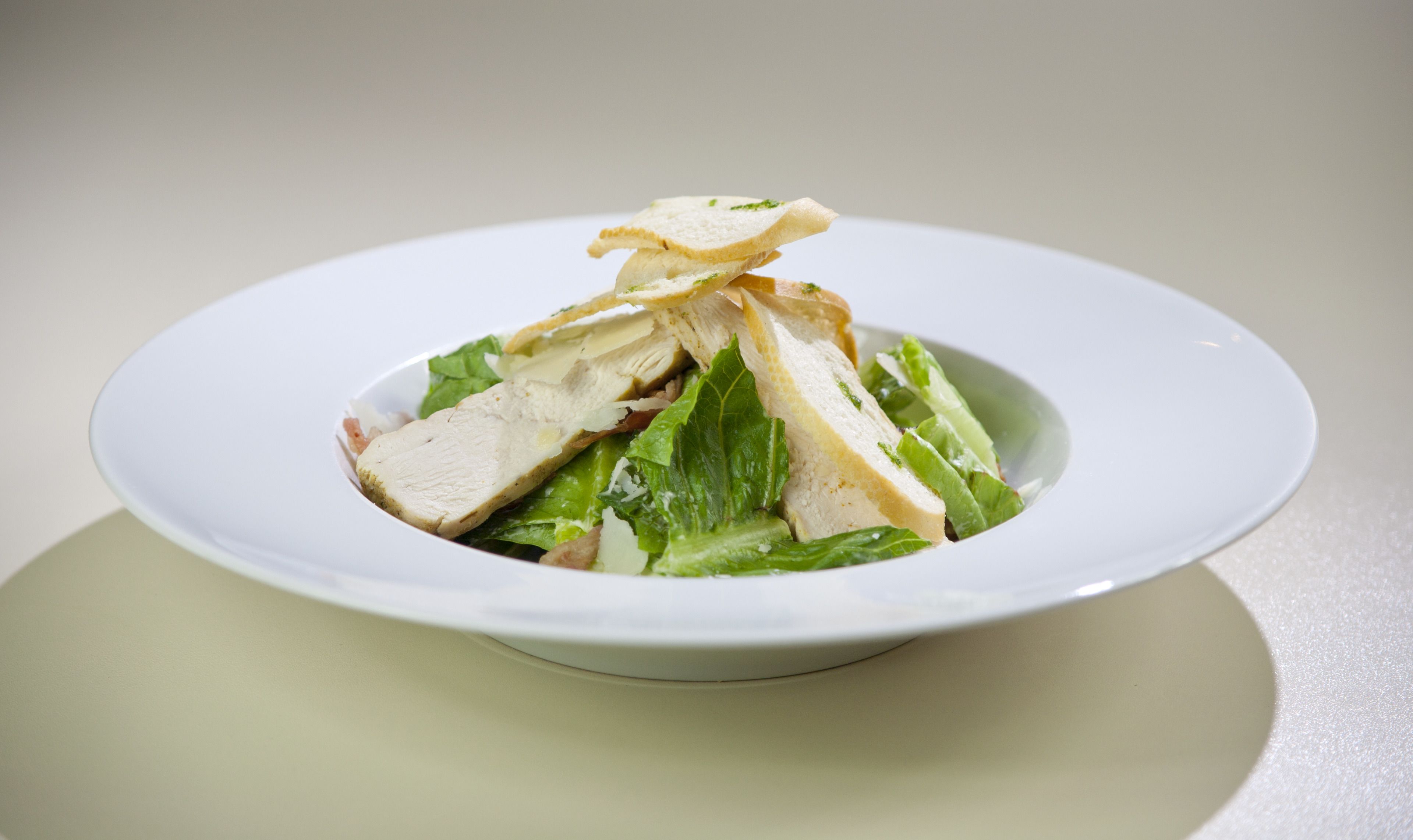 A white plate with a salad consisting of lettuce, chicken, and croutons.