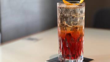 Ein hoher, strukturierter Glasbecher gefüllt mit einem roten Getränk und Eiswürfeln, mit einer Orangenscheibe verziert, auf einem Untersetzer.