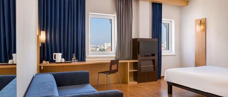 Habitación de hotel con cama, escritorio con computadora, silla, televisión y ventana con cortinas.