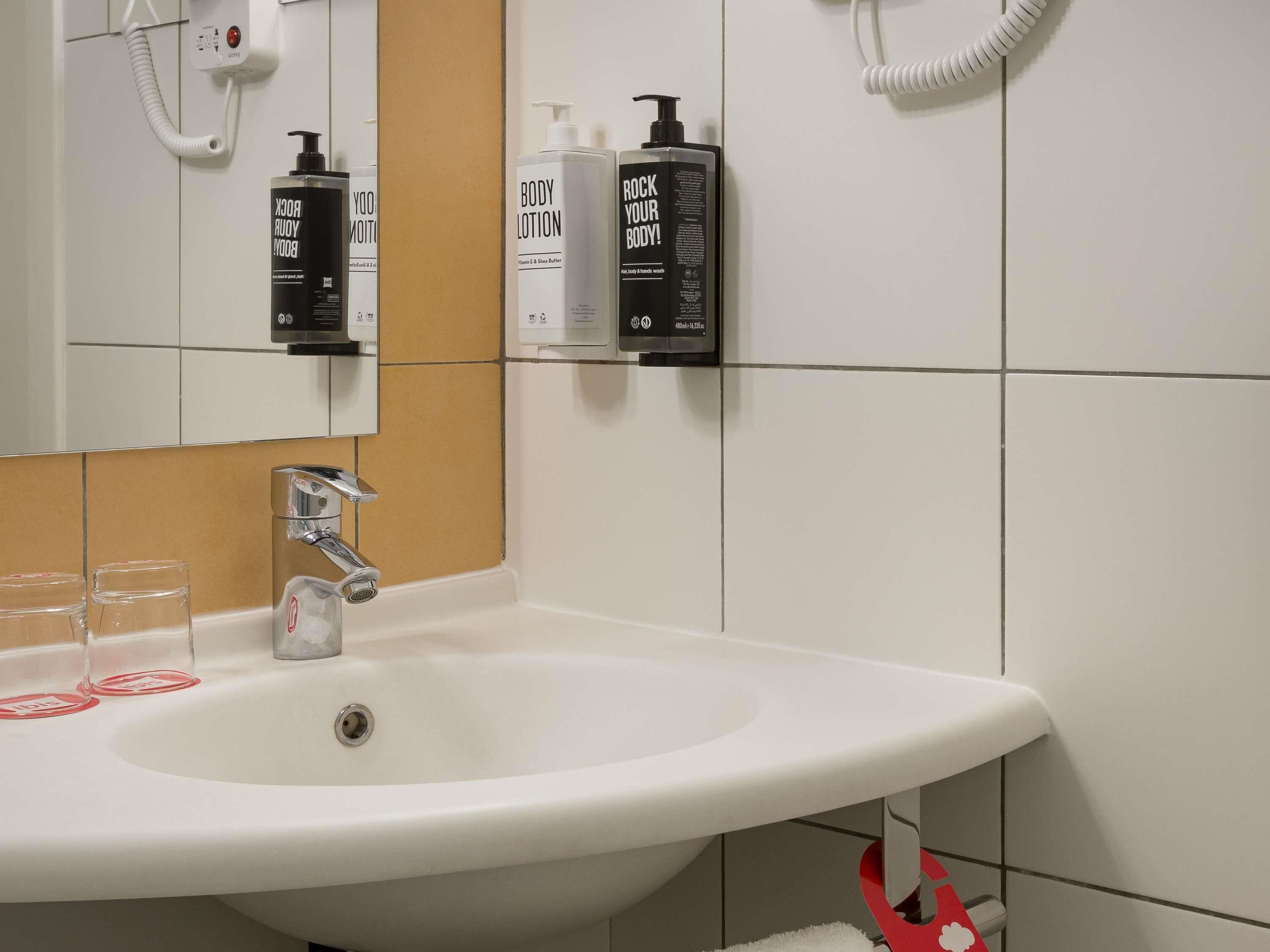 Un baño con lavamanos blanco, un espejo y dos botellas de crema corporal en la pared.