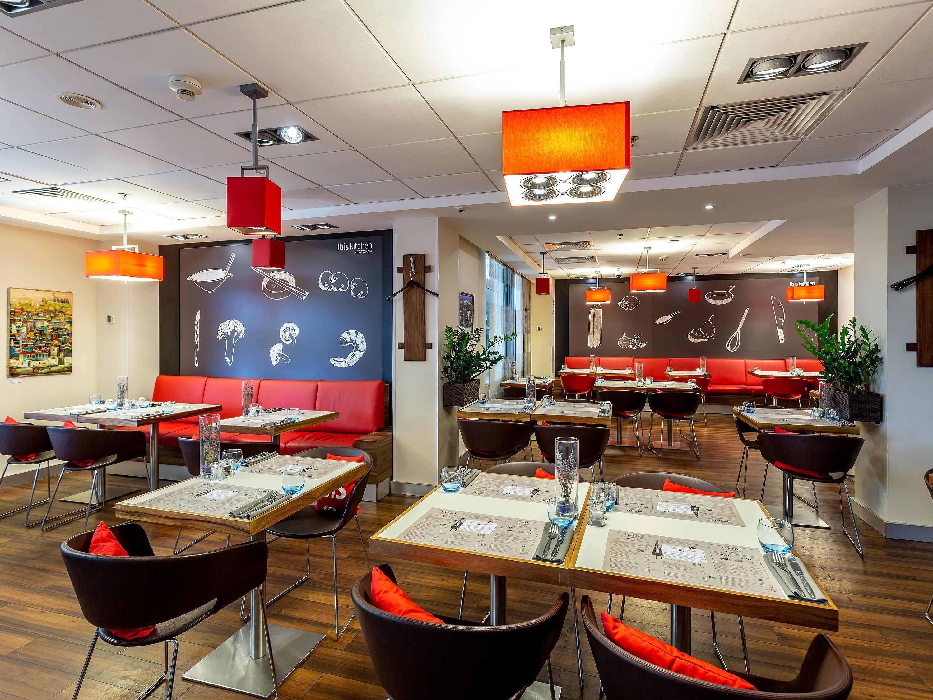 A modern restaurant interior with multiple dining tables, red cushioned booths, and pendant lighting.
