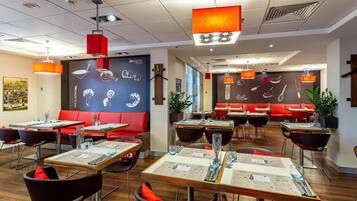 A modern restaurant interior with multiple dining tables, red cushioned booths, and pendant lighting.