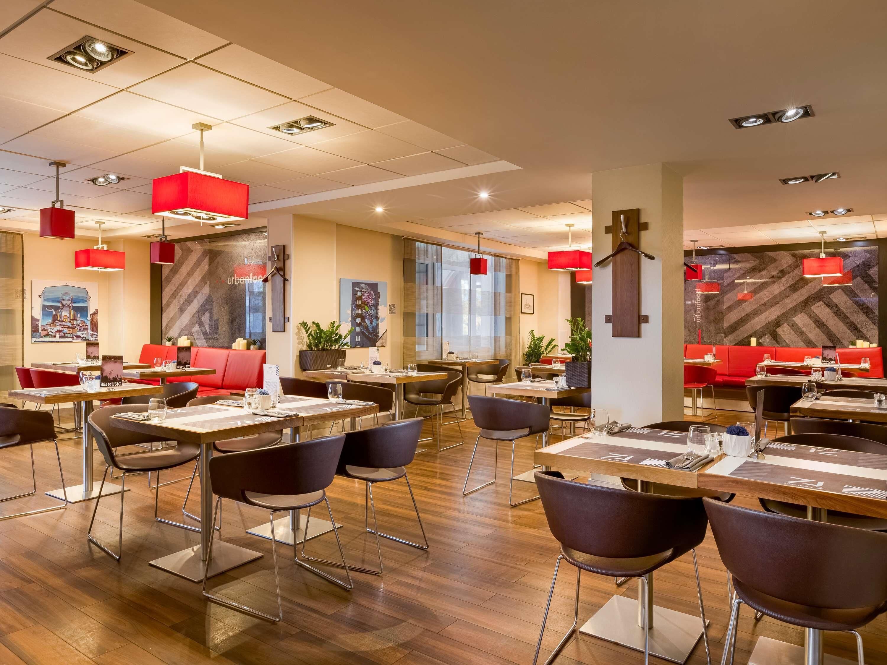 A modern restaurant interior with wooden flooring, red seating, and pendant lighting.