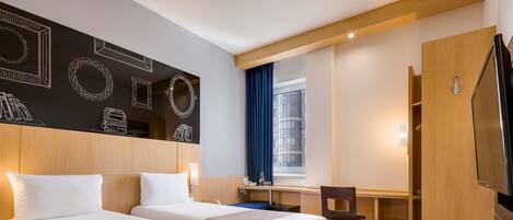 A hotel room with two beds, a desk, a chair, a TV, and a window with curtains.