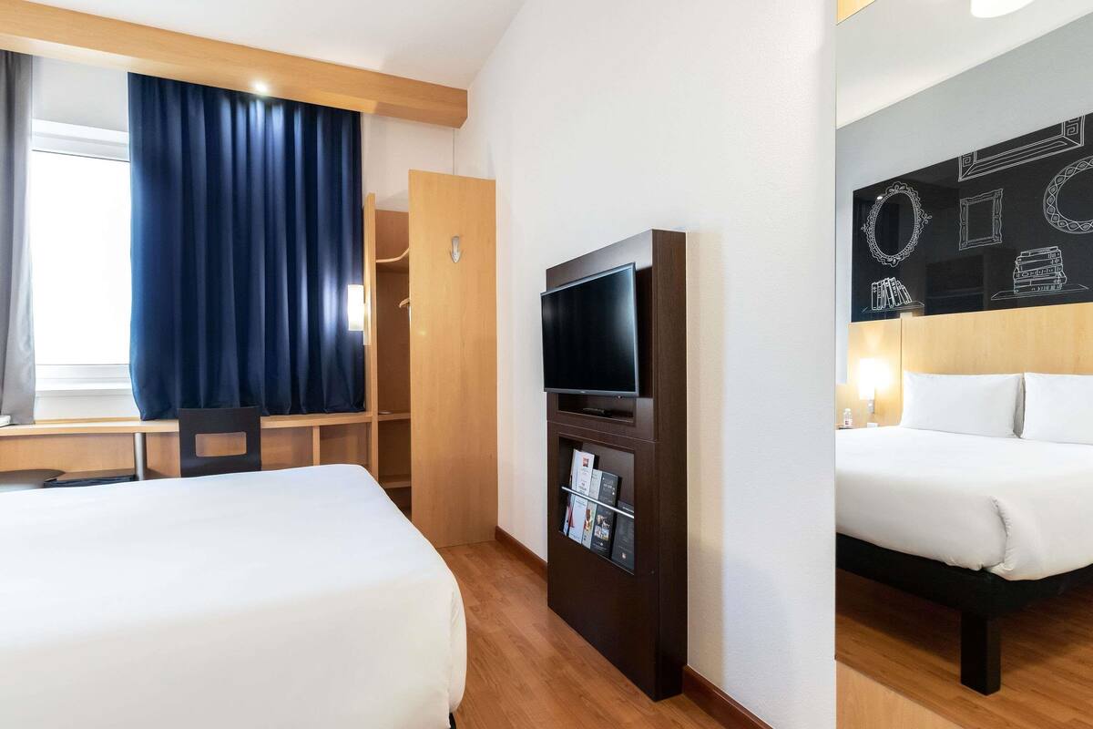 A hotel room with two beds, a flat-screen TV, a desk, and a wardrobe.