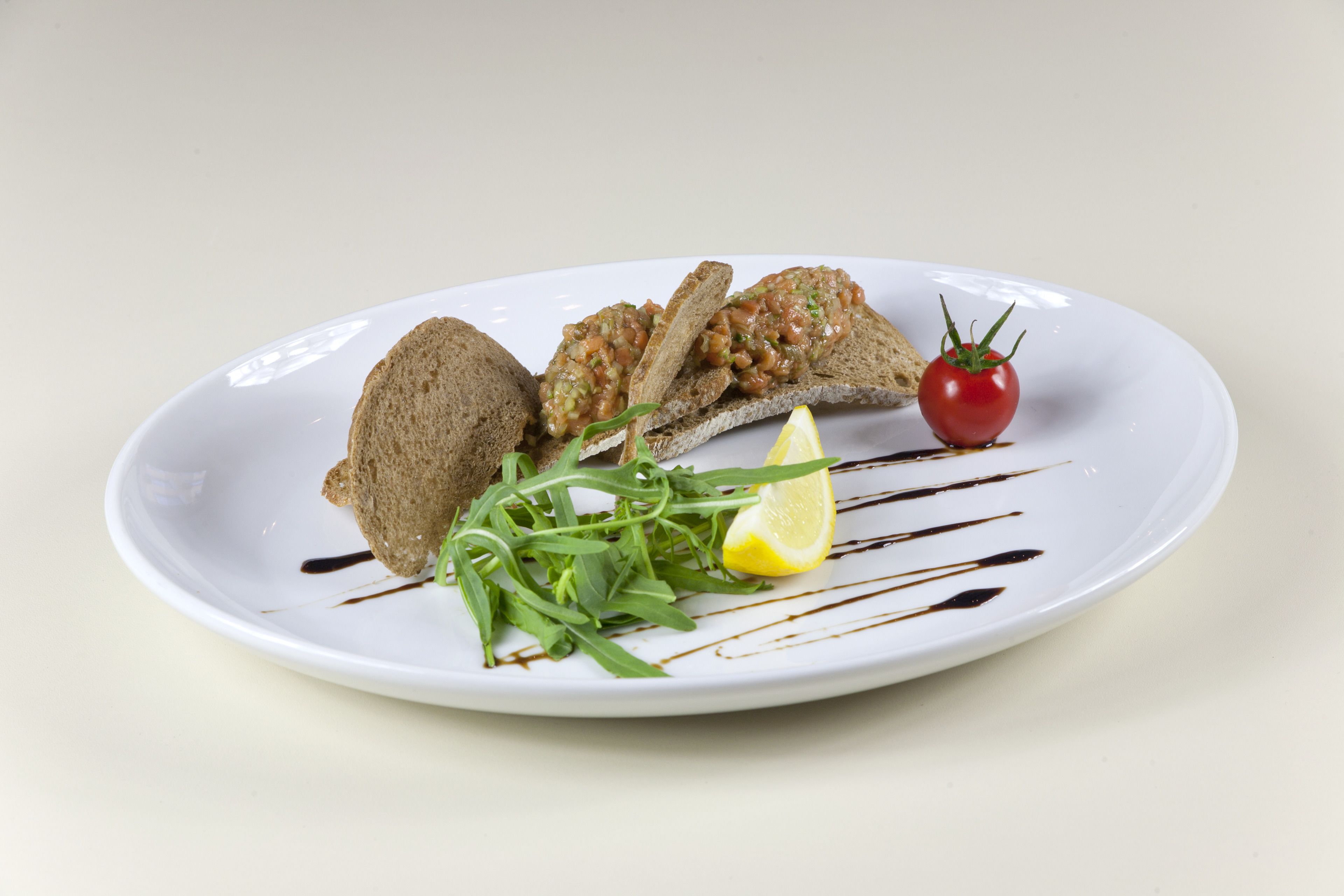 A plate with bread, tomato, lemon, and greens.