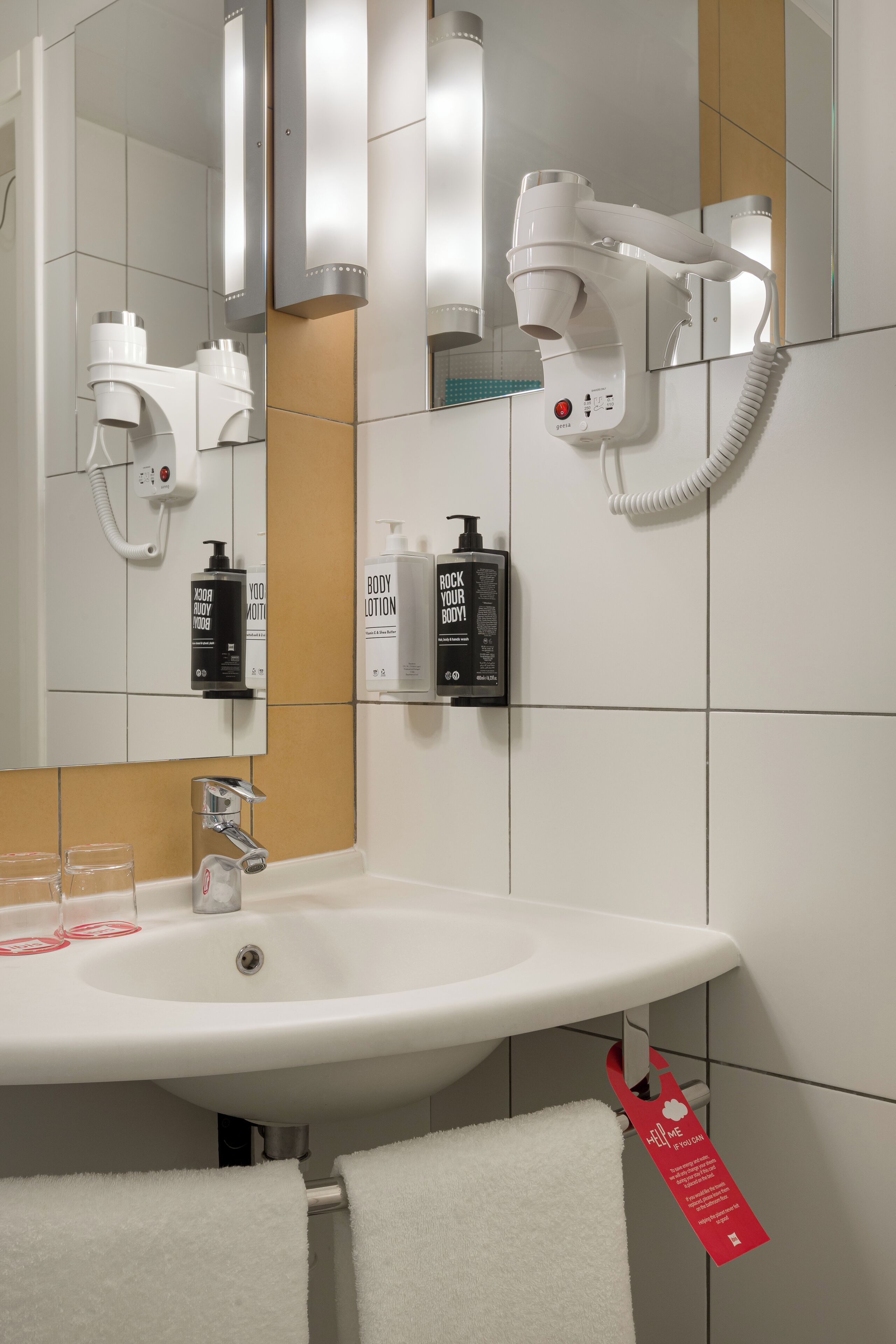 Ein modernes Badezimmer mit einem weißen Waschbecken, einem Fön und Pflegeprodukten.