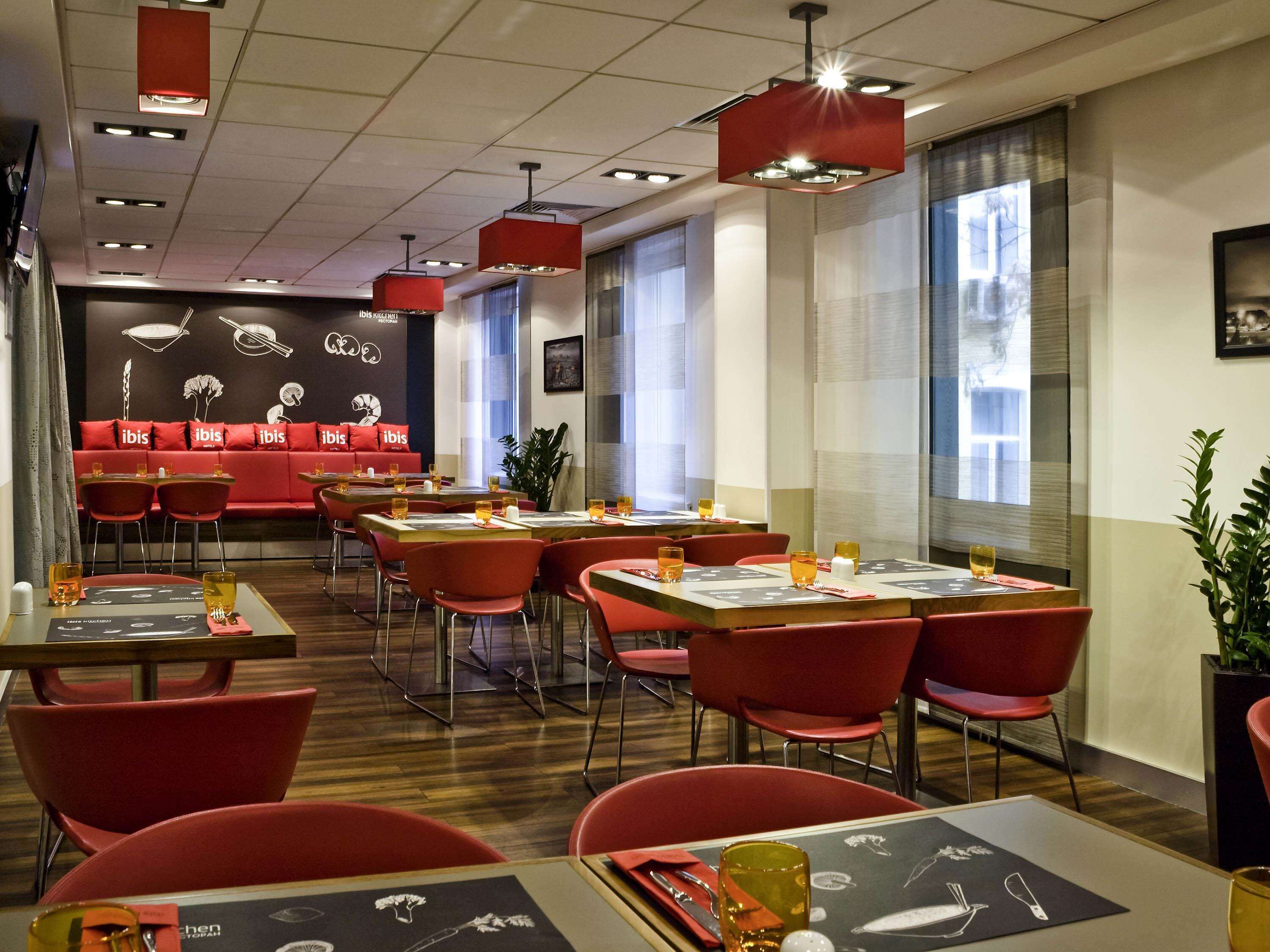 Ein Restaurant mit roten Stühlen und Tischen, einem roten Sofa mit 'ibis'-Branding und einer Speisekarte mit Illustrationen von Speisen.