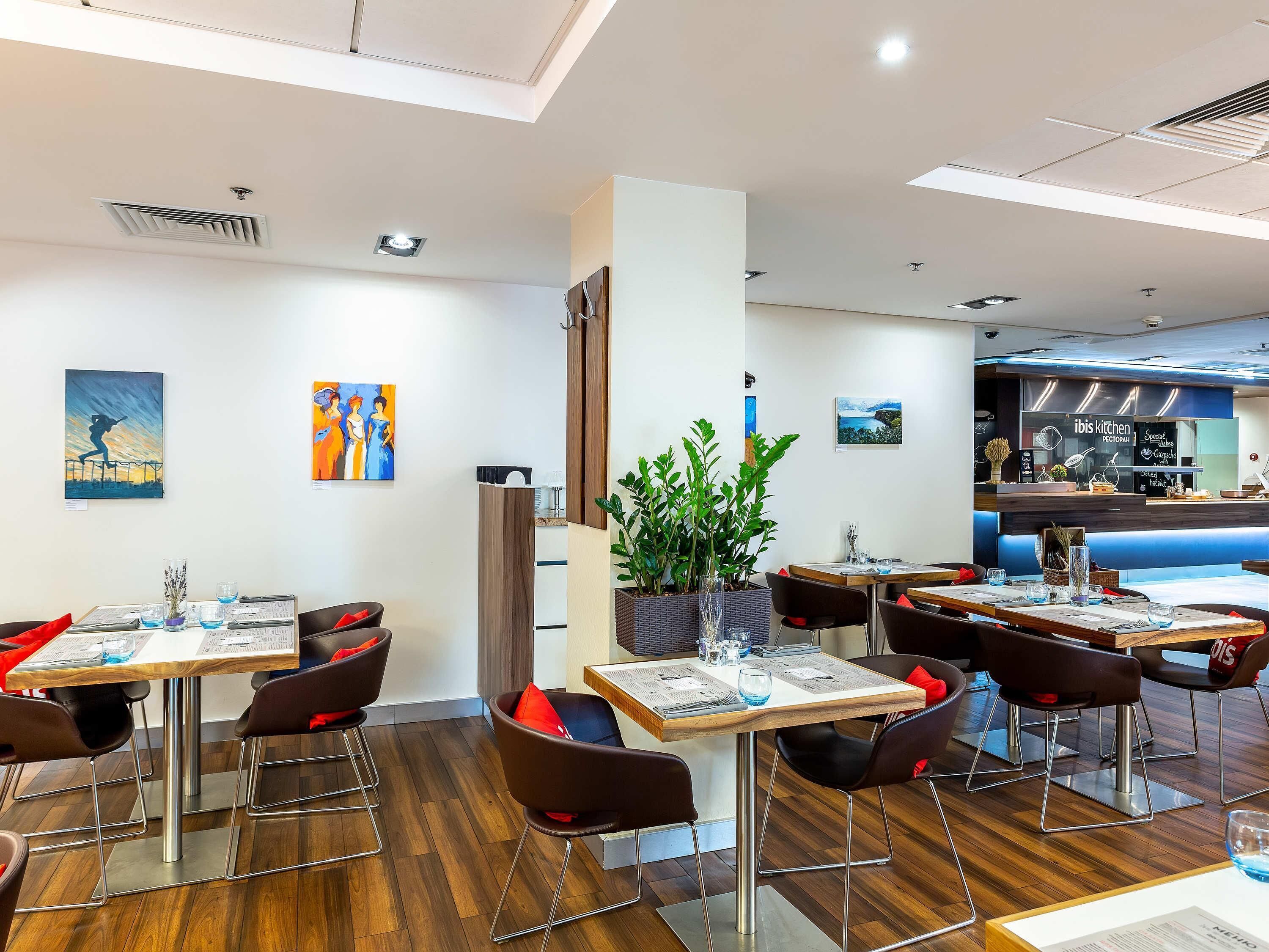 Een modern restaurantinterieur met houten tafels, zwarte stoelen en een grote plant in het midden.