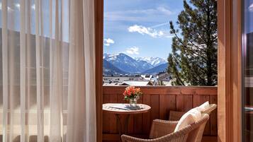 Un balcón con una silla de mimbre, una mesita redonda con un florero y vistas a montañas nevadas.