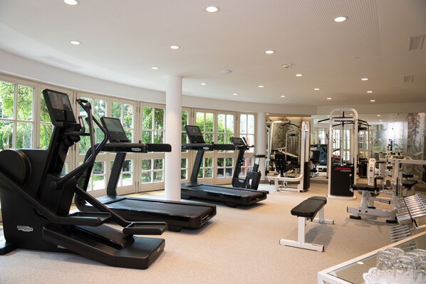 Une salle de sport équipée de tapis de course, d’appareils de musculation et d’un banc.