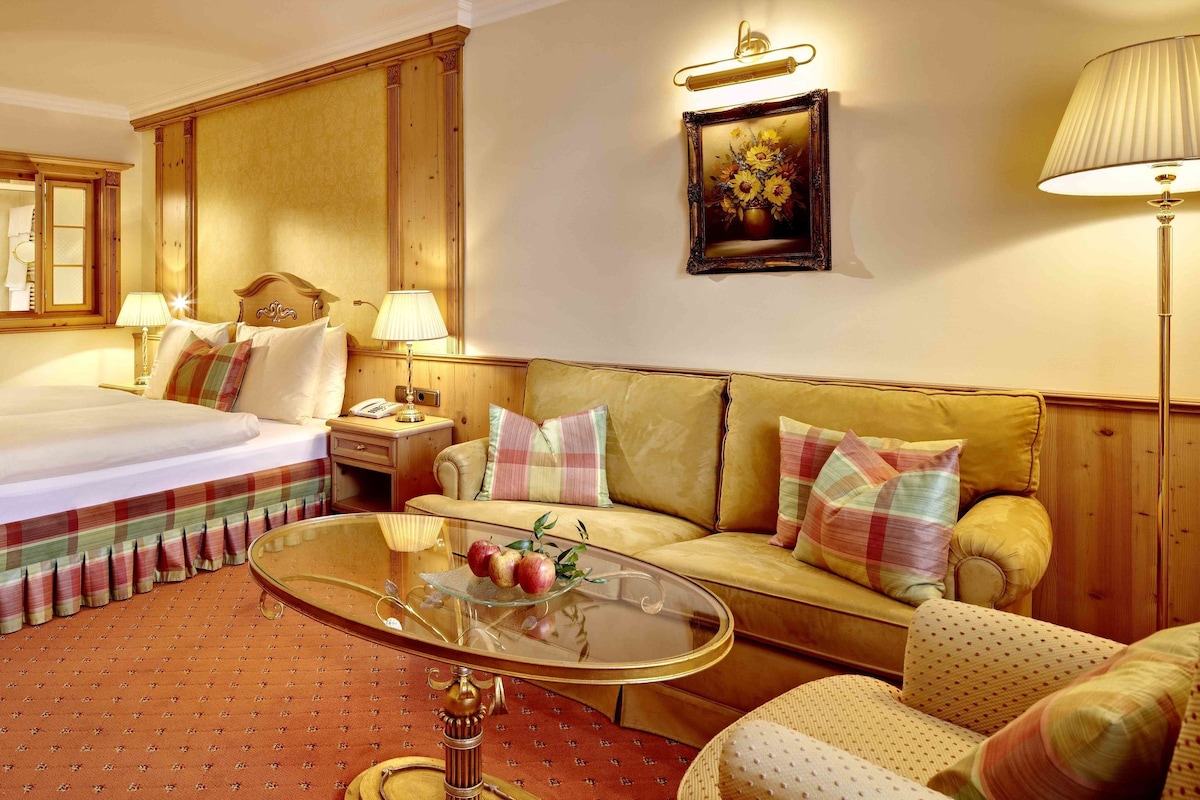 Une chambre d’hôtel avec un lit, un canapé, une table basse en verre, une lampe et un tableau au mur.