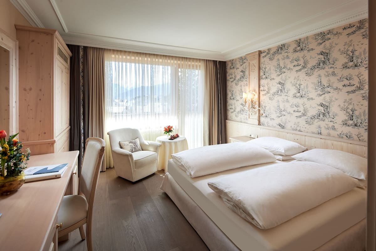 Een hotelkamer met een groot bed, een bureau, een stoel en een tafeltje met een bloevas.