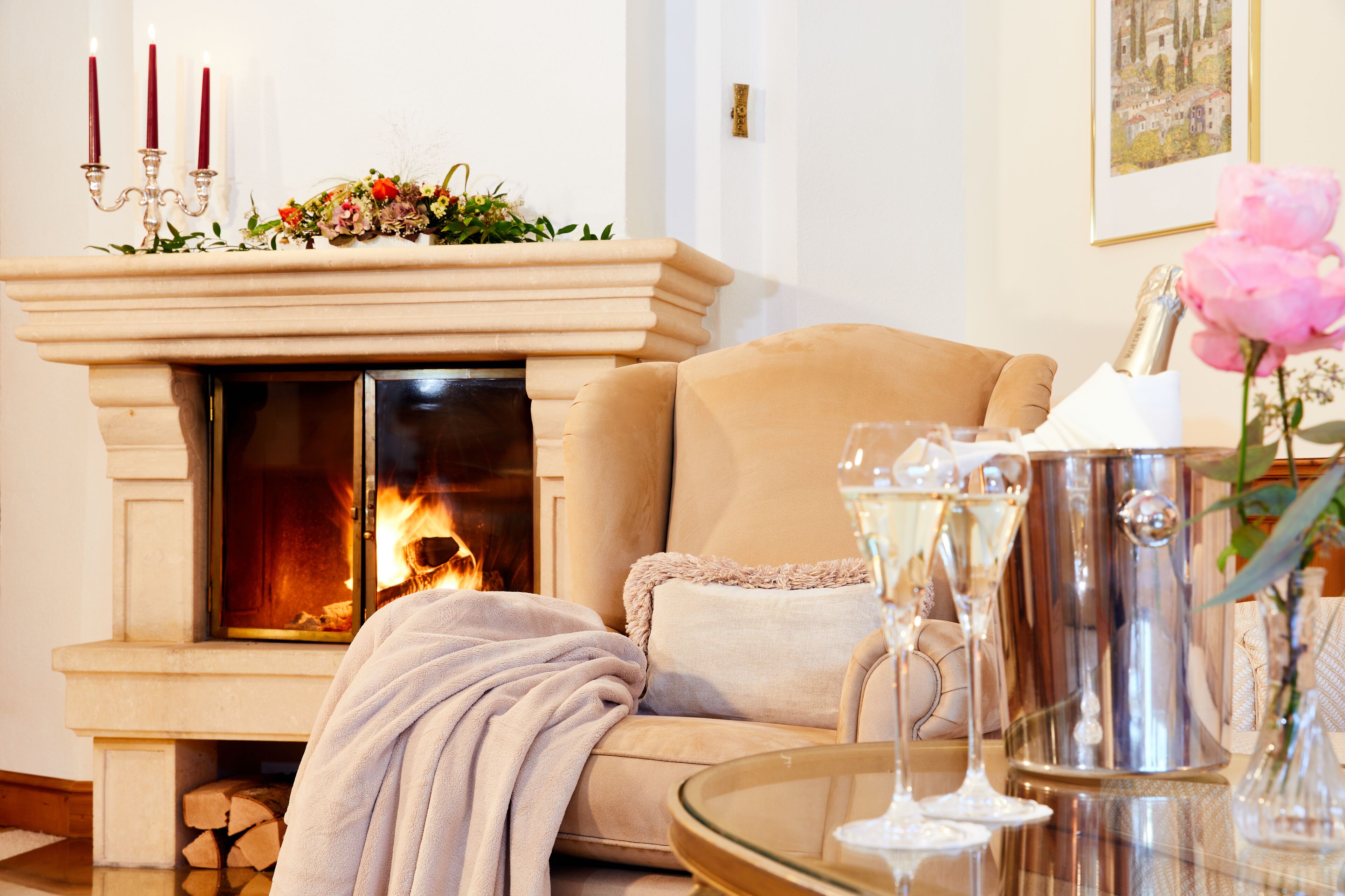 A cozy living room with a fireplace, a sofa, and a table with glasses and a flower vase.