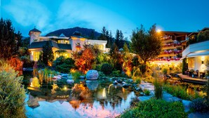 Un hotel con un estanque en el jardín, senderos de piedra y una montaña al fondo.