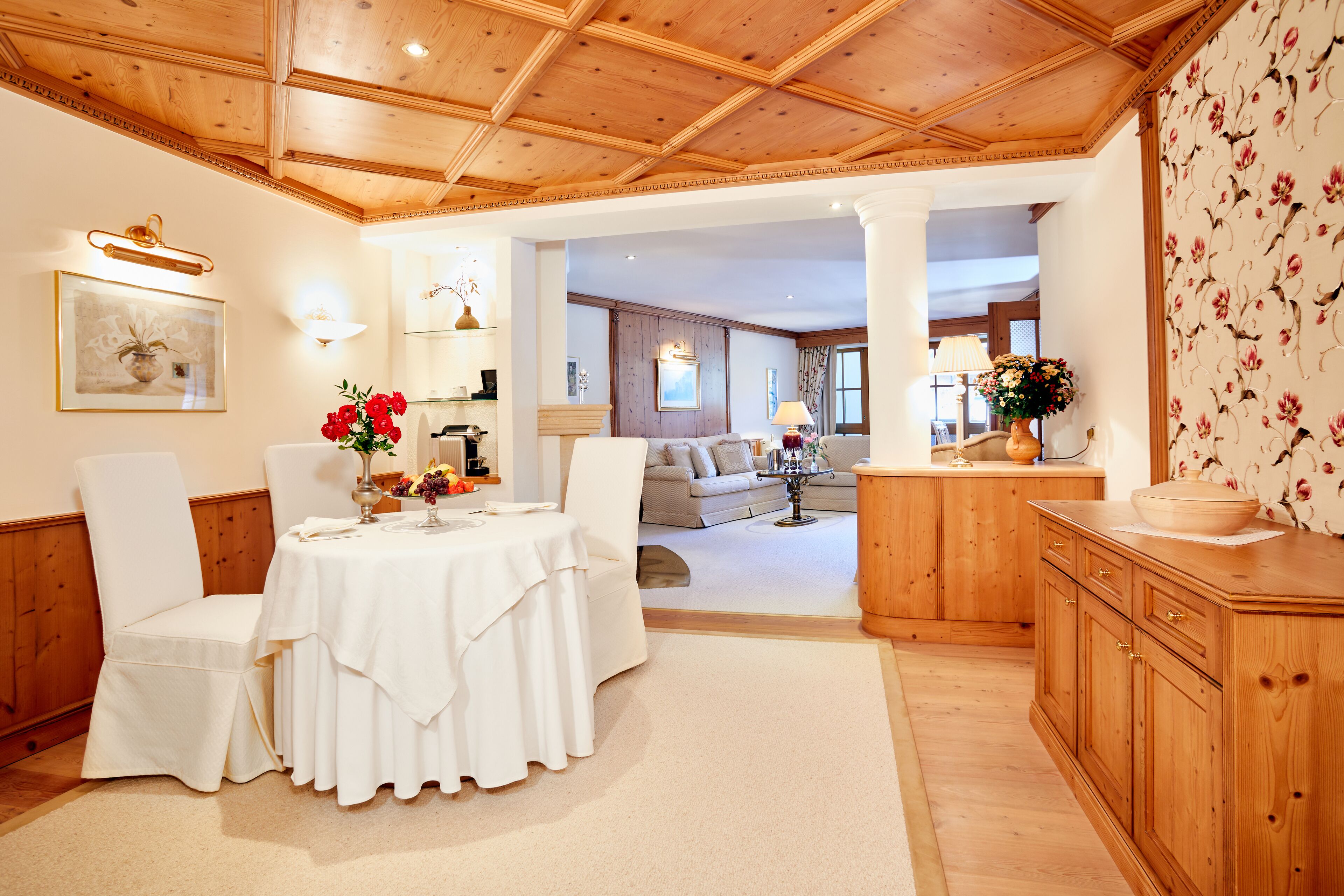 Un comedor con una mesa preparada para dos, un armario de madera y una pared cubierta de papel tapiz floral.