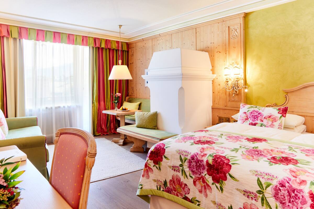 Een hotelkamer met een bed, een bureau, een stoel, een tafel met bloemen en een raam met gordijnen.