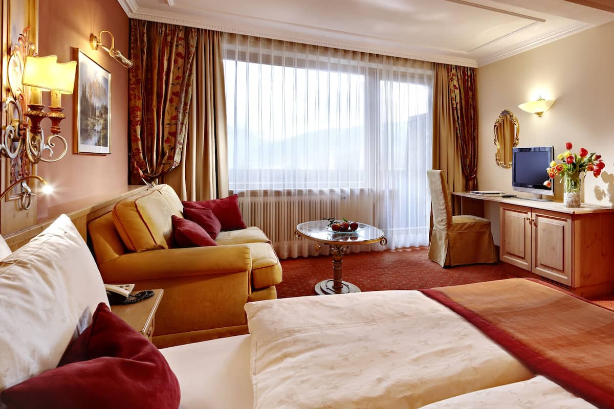Een hotelkamer met een bed, een slaapbank, een bureau, een televisie en een badkamer die door een open deur zichtbaar is.
