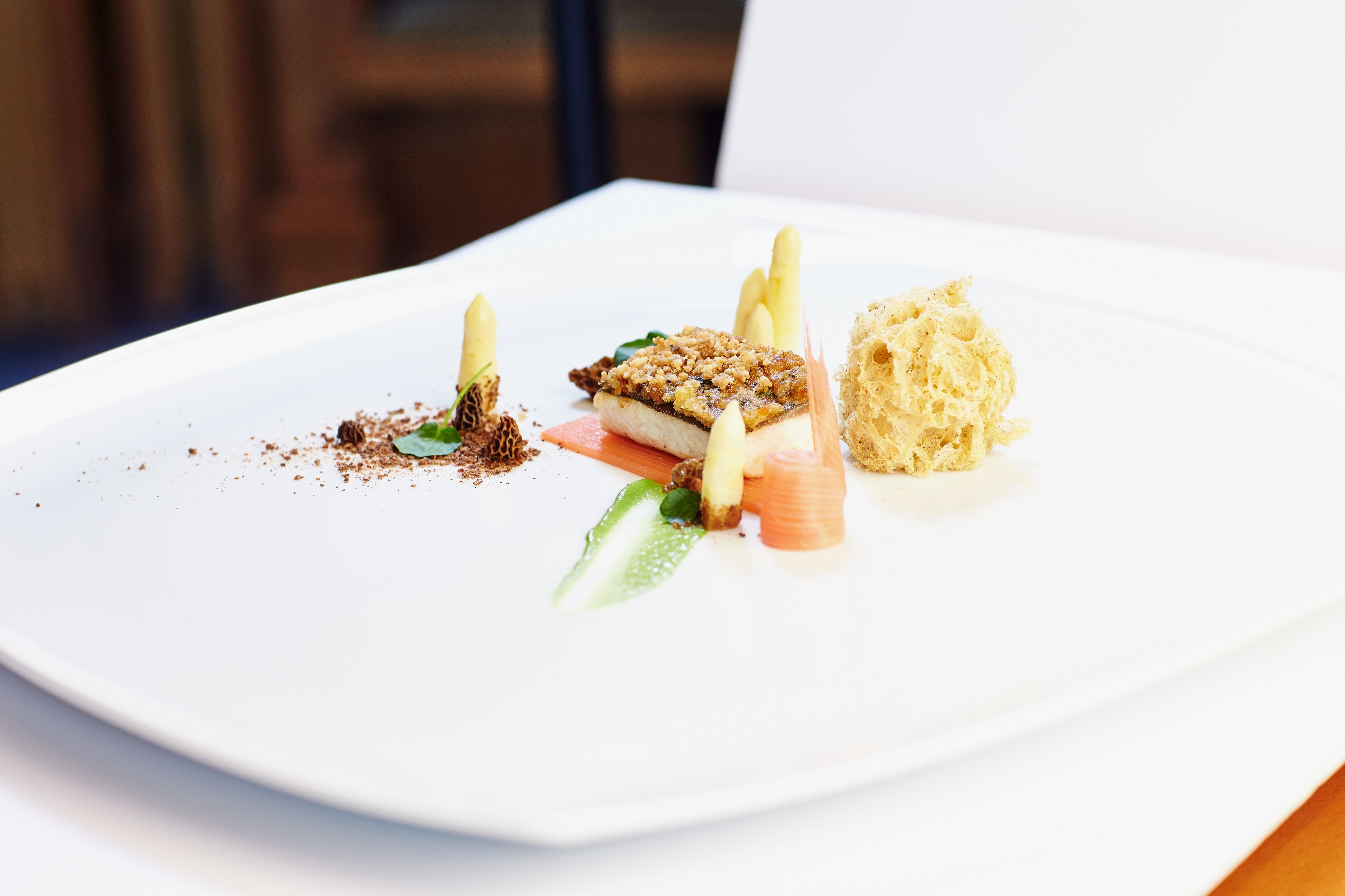 A white plate with a variety of food items, including a piece of fish, some vegetables, and a small mound of what appears to be a dessert.